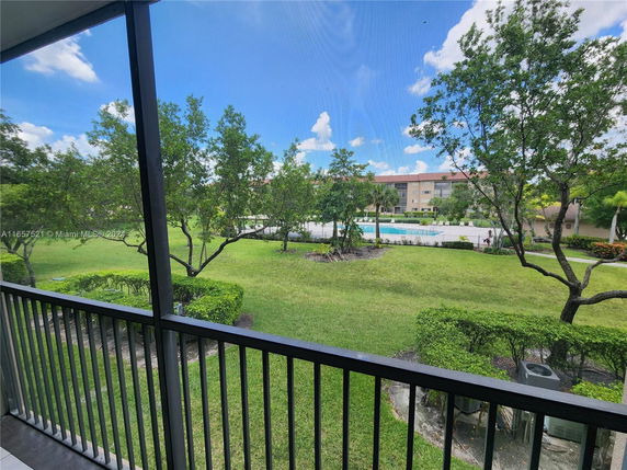 View from a balcony overlooking a landscaped area with trees and a swimming pool in the background.