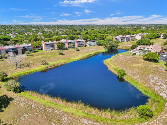 Aerial view of buildings near a large pond with surrounding greenery.