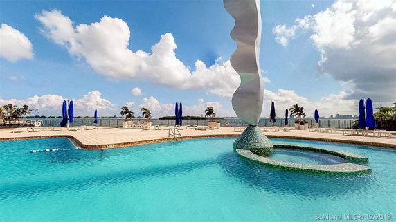 View of an outdoor swimming pool with a unique sculpture in the center and loungers around the pool area.