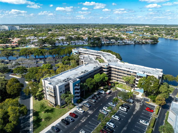 Aerial view of a multi-story building near a lake with surrounding residential area.