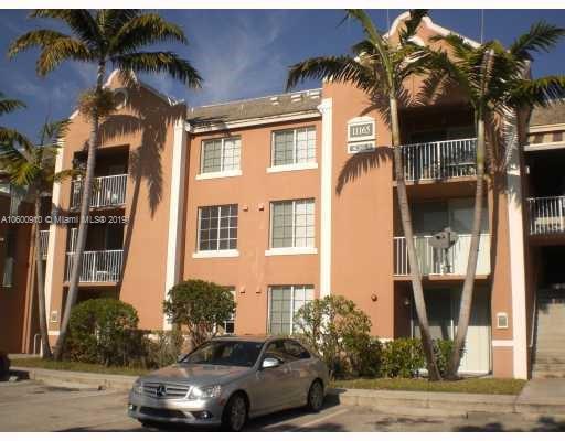Front view of a three-story apartment building with balconies and a parking area.
