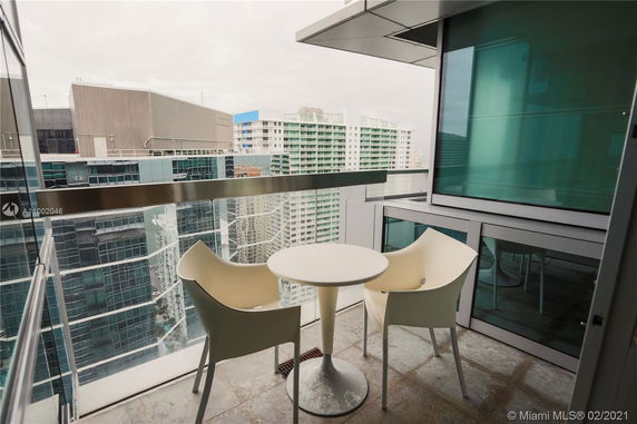View from a balcony with two chairs and a table, overlooking tall buildings.