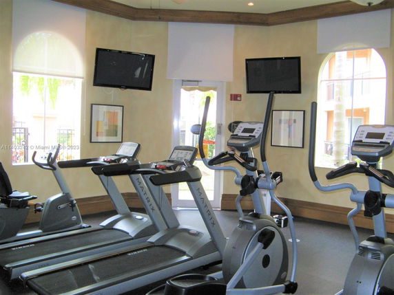 Indoor gym area with exercise machines and wall-mounted TVs.