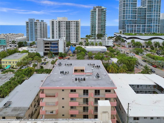 Rooftop view featuring AC units on a mid-rise building overlooking a coastal cityscape with other tall buildings and ocean in the background.