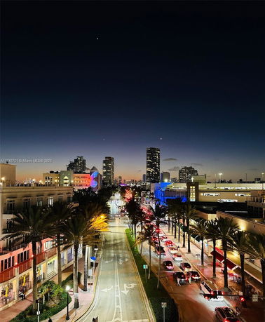 Panoramic evening view of a city street with buildings and traffic lights.