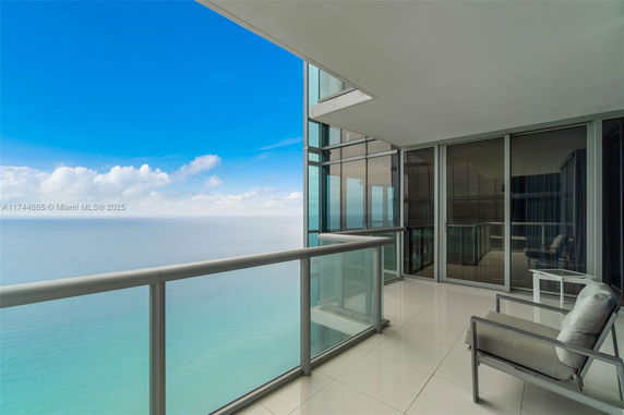 Balcony with glass railing offering a panoramic view of the sea and sky.