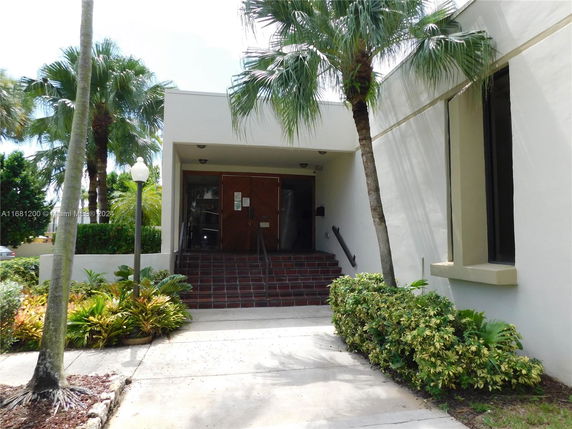 Front view of a building entrance with stairs and palm trees.