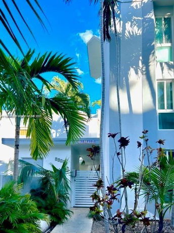 Front view of a building with palm trees and a white gate entrance.
