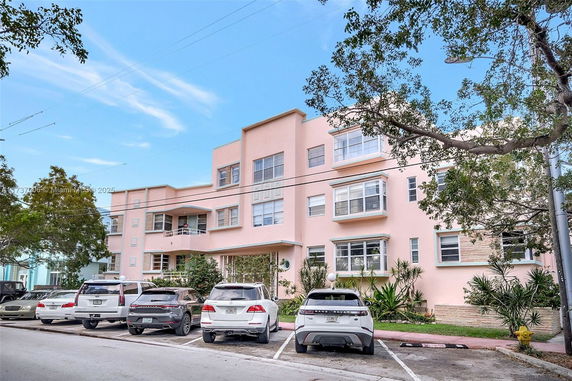 Front view of a multi-story building with multiple windows and parked cars.