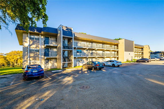 Outdoor view of a multi-story residential building with parking spaces filled with cars in front.