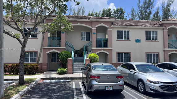 Front view of a two-story residential building with arched balconies and parking area in front.