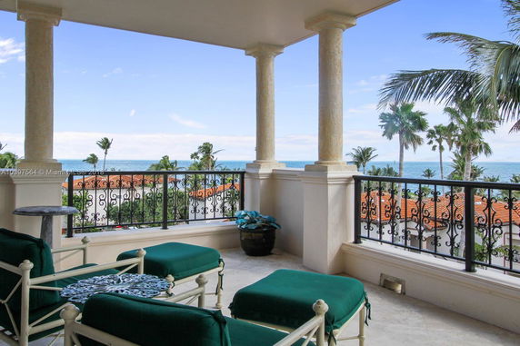 Balcony view overlooking the ocean with palm trees and terracotta roofs.