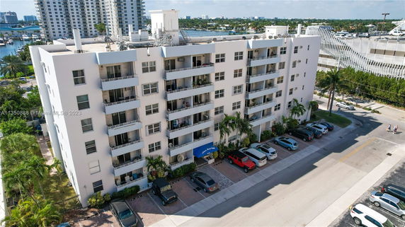 Front view of a multi-story apartment building with balconies and a parking area.