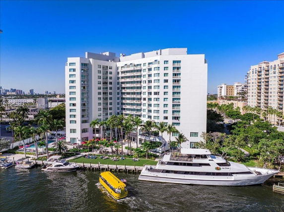 Front view of a multi-story hotel building by the waterfront with a boat docked nearby.