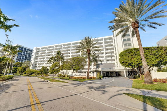Front view of a multi-story building with balconies and palm trees.