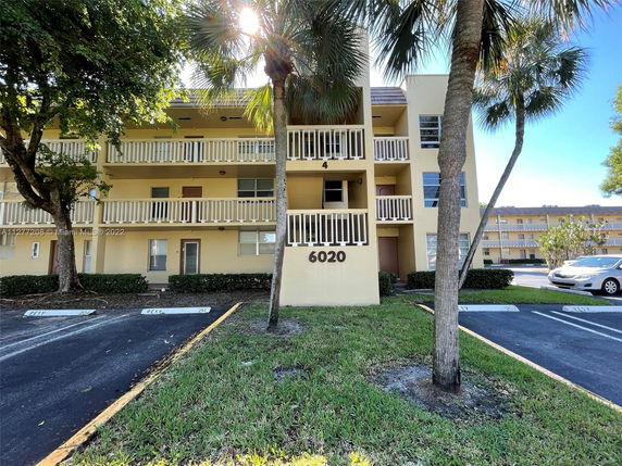 Front view of a multi-story residential building with balconies and parking spaces.