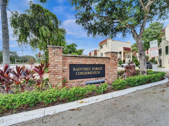 Entrance sign of Raintree Forest Condominium with surrounding buildings.
