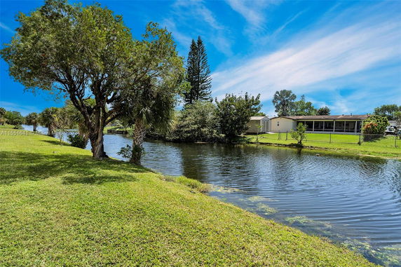 Scenic view of a water body surrounded by grassy banks and trees, with a residential house visible in the background.