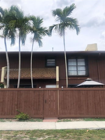 Front view of a two-story house with a wooden fence and palm trees.