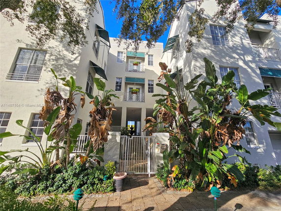 Front view of a multi-story residential building with balconies and plants in front.