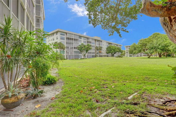 View of a large multi-story residential building with balconies and windows, surrounded by a grassy area and trees.