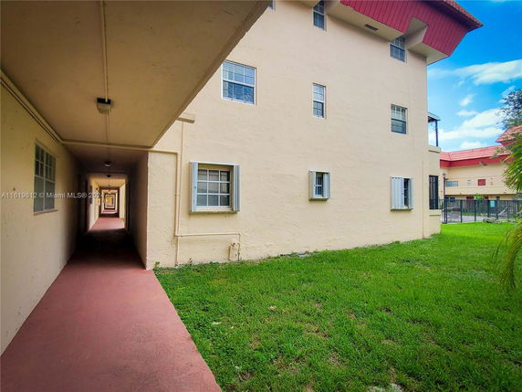 Exterior view of a multi-story building with red roofing and a covered walkway adjacent to a grassy area.