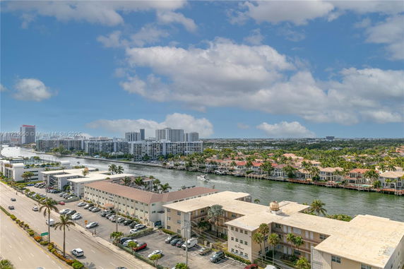 Panoramic view of a waterway with residential and commercial buildings, roads, and palm trees during the daytime.