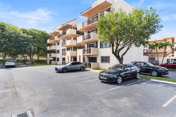 Parking area in front of a multi-story residential building with cars parked.