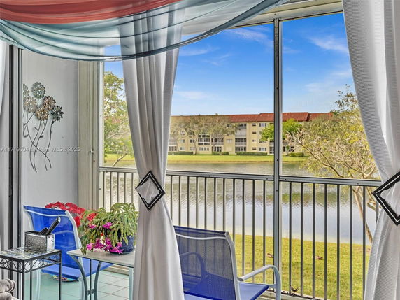 Screened balcony with chairs and a table overlooking a lake and distant building.