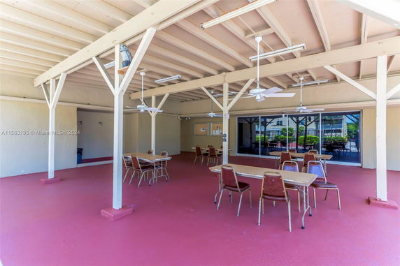 Indoor area with multiple tables and chairs, wooden ceiling beams, and ceiling fans.