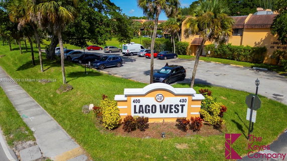 Outdoor parking area with scattered parked vehicles and a sign for Lago West.