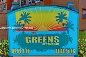 Sign for a residential community named 'The Greens of Tamarac' featuring palm trees and a sunset design.