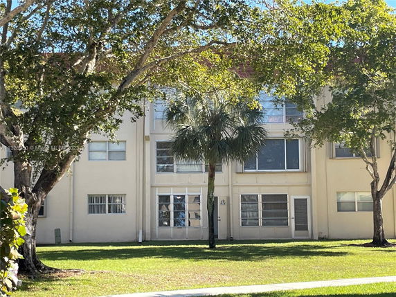Front view of a two-story residential building with large windows and surrounded by trees.