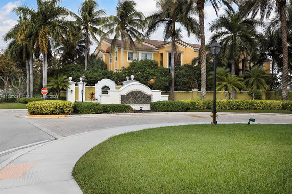 Front view of a large multi-story house with yellow walls and palm trees.
