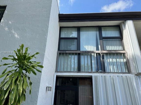 Front view of a multi-story house with large windows and a plant nearby.