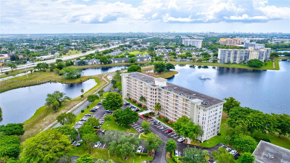 Aerial view of a multi-story residential building near a body of water, surrounded by trees and roads.