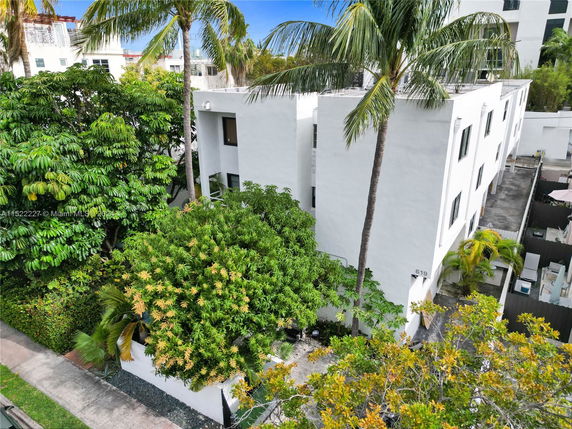 Front view of a modern, multi-story white building surrounded by palm trees.