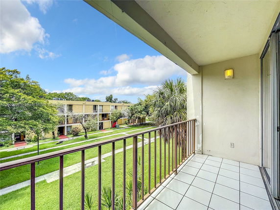 View from a balcony overlooking a grassy area and adjacent apartment buildings.
