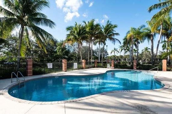 Swimming pool area with palm trees and a fenced perimeter.