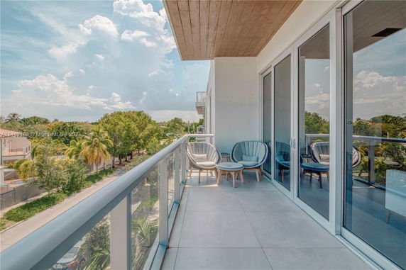 Balcony view with outdoor seating and a glass railing, overlooking trees and a road.