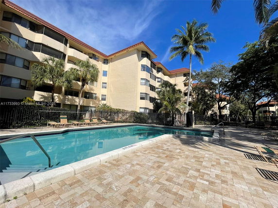 Outdoor swimming pool area adjacent to a multi-story residential building.