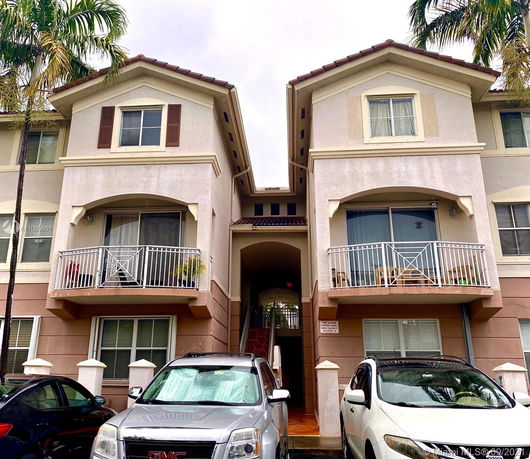 Front view of a multi-story residential building with balconies and parking space in front.