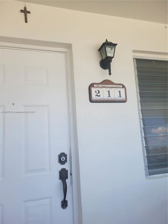 Front view of a house entrance with a door, window, house number plaque, and wall-mounted lantern.