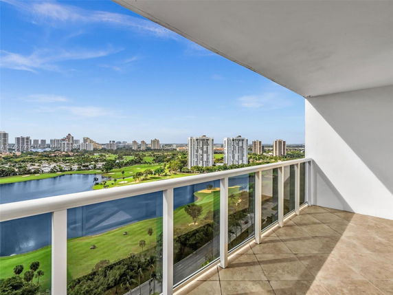 Panoramic view from a balcony overlooking a golf course, water features, and city buildings.