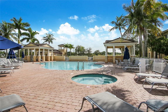 Outdoor area with a swimming pool and jacuzzi, surrounded by lounge chairs and umbrellas.