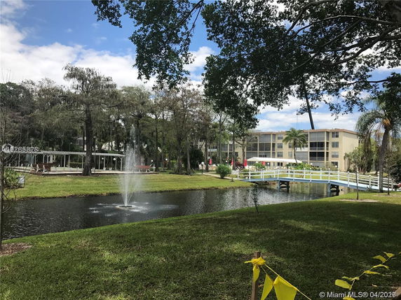 View of a building complex with a pond, fountain, and bridge in the foreground.