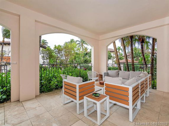 Covered outdoor seating area with chairs and cushions, overlooking a garden with trees.