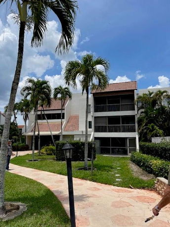 Front view of a multi-story building with balconies and palm trees in front.