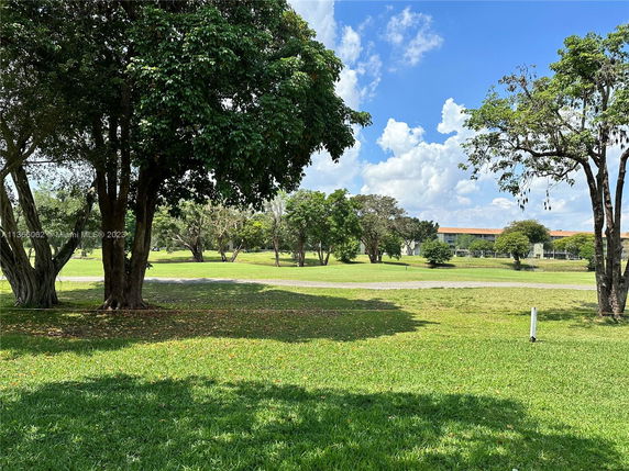 Open grassy area with trees and a distant view of residential buildings.