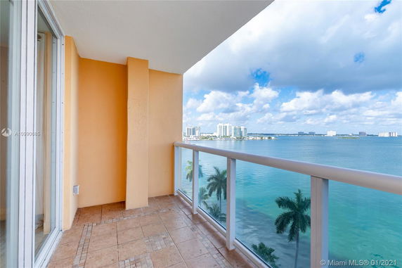 Balcony view overlooking a large body of water with distant buildings and a clear sky.
